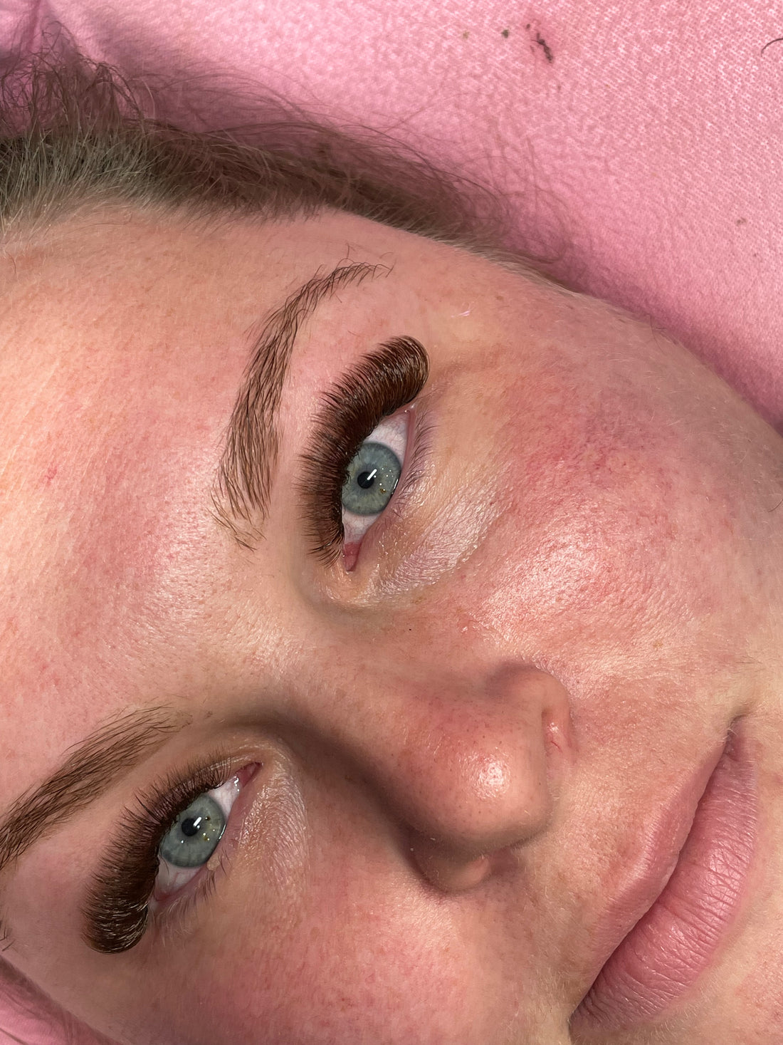 Close-up of woman with premium lash extensions on pink towel, Leo Lash Range
