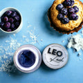 Leo Lash professional lash supplies container with purple lash extension cream, blueberries, and muffin on blue background